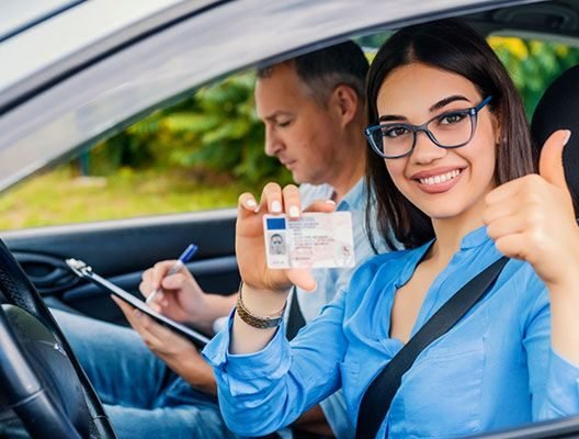 Smiling driver holding a license and giving a thumbs-up beside an instructor